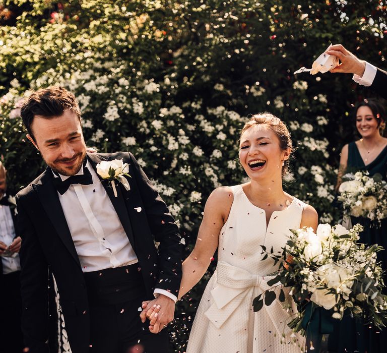 Bride & groom walk through confetti whilst laughing on their wedding day