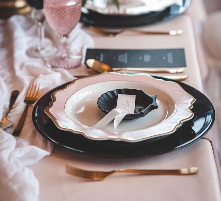 Place setting with black and gold rimmed tableware, and an ornate shell plate 