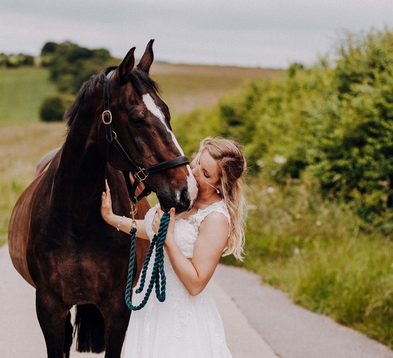 Bride stands with her horse on her wedding day as they walk along the road