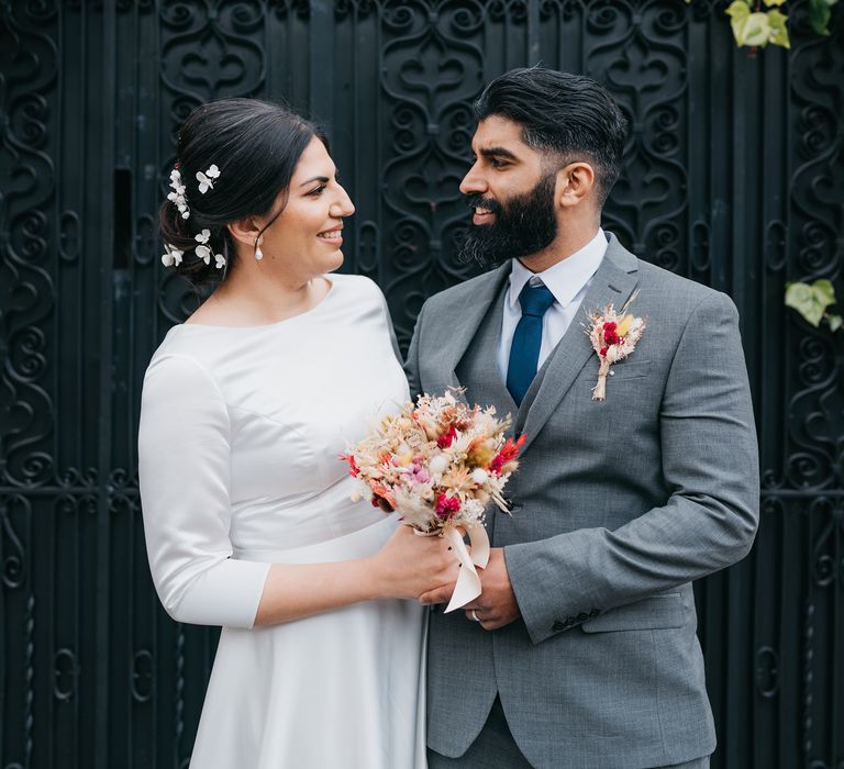 Bride & groom look lovingly at one another as groom wears Ted Baker suit and matching buttonhole to floral bouquet