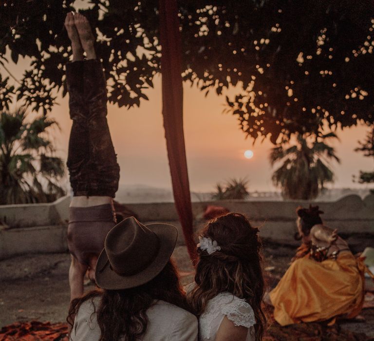 Bride & groom sit on Moroccan style rugs as they watch the sun set with their wedding guests in the Sicilian countryside 