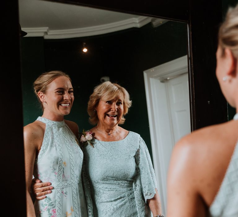 Bride looks in the mirror with her mother on the day of her wedding as they smile at one another