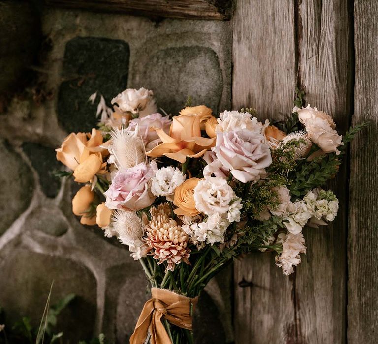 Wedding bouquet with blush pink and yellow peeled back roses tied with ribbon