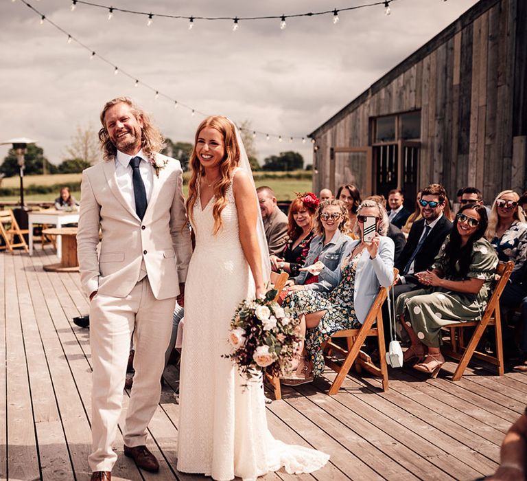 Bride clutches artificial wedding bouquet at she stands with her groom during ceremony