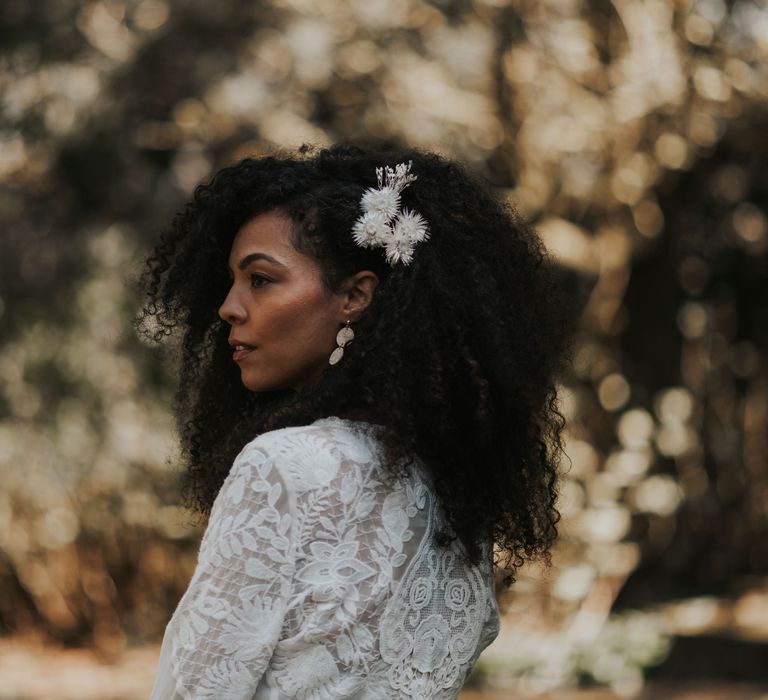 Black bride with afro hair wearing a white flower hair accessory and lace wedding dress 