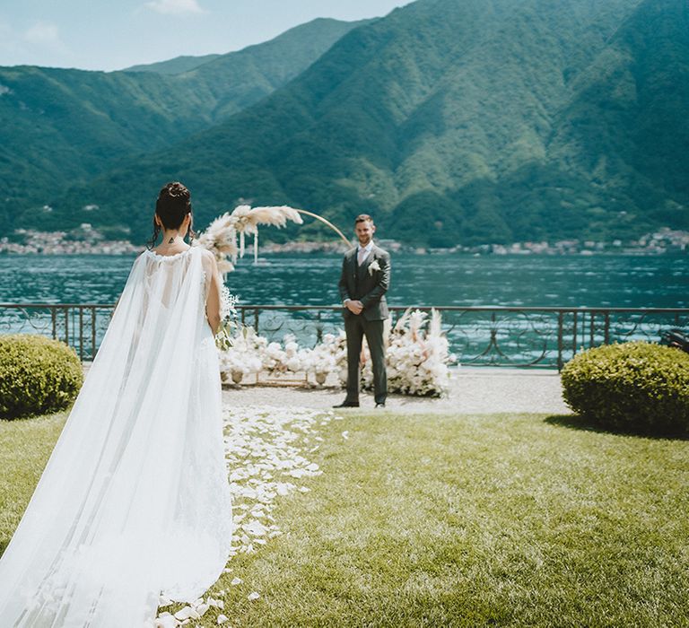 Bride walks toward her groom in bespoke gown with gossamer cape