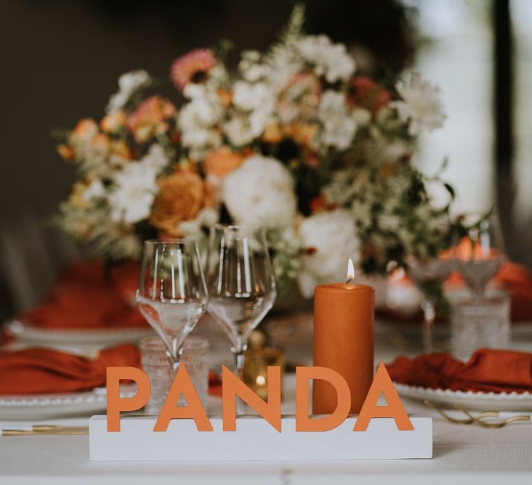 PANDA wedding table name sign with orange pillar candle and centrepiece flowers 