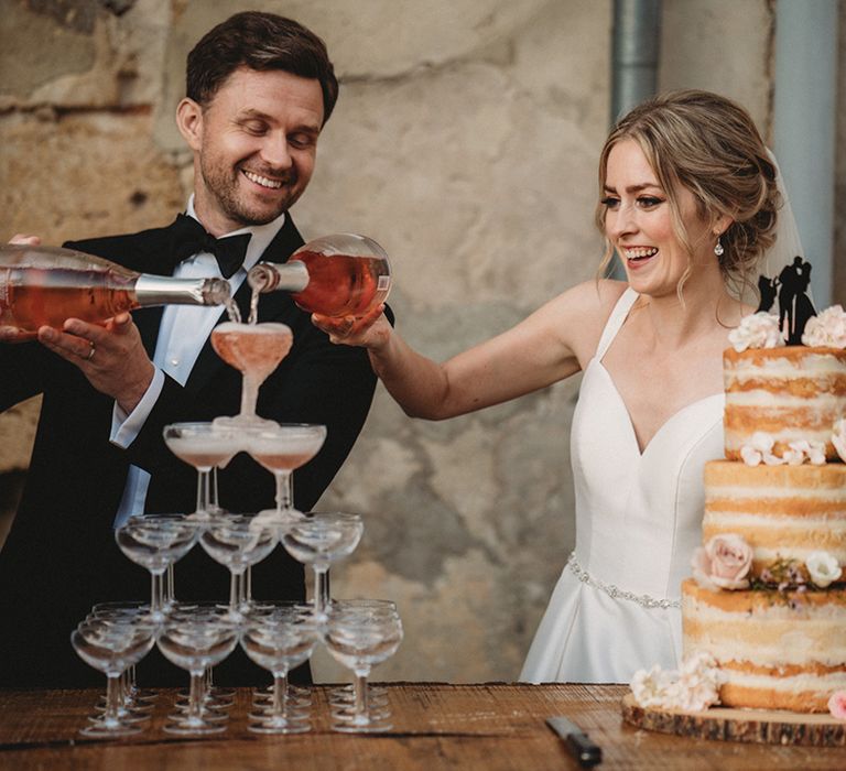 Bride and groom cutting the naked wedding cake and pouring drink into the champagne tower 