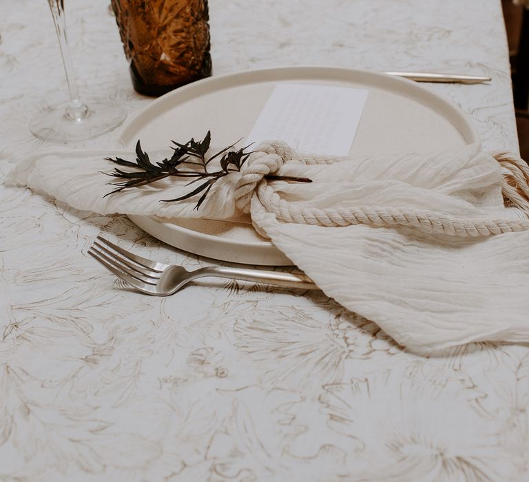 Place setting with ceramic charger plate and linen napkin tied with rope 