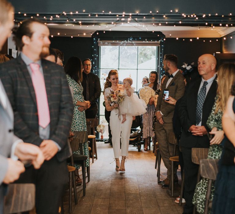 Bridesmaid in jumpsuit carries flower girl down the aisle at Georgian town house Norwich wedding