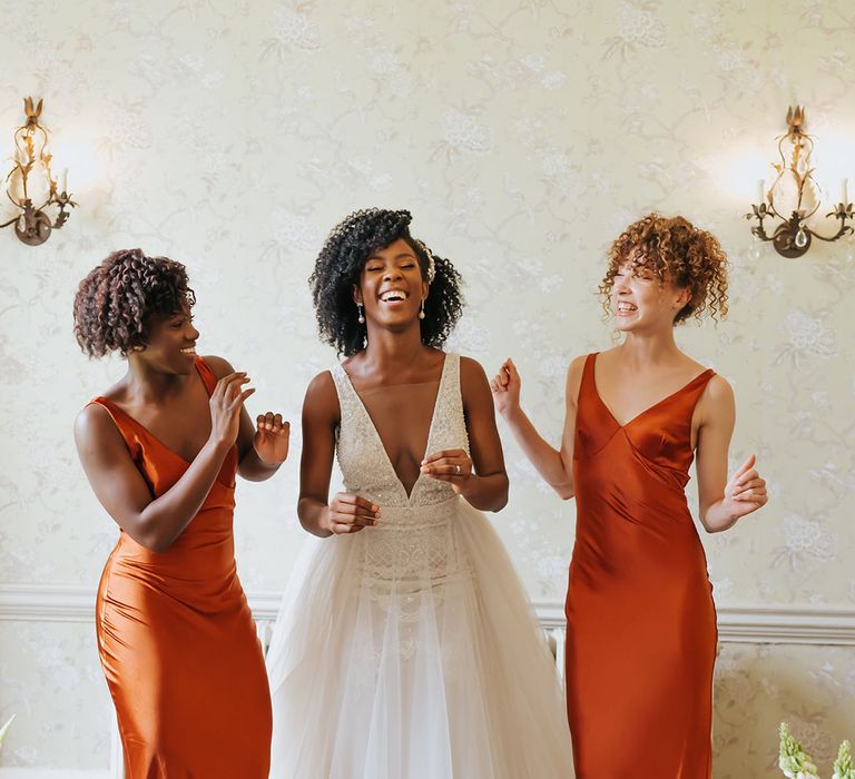 Bride and bridesmaids in orange satin dresses laughing at stylish Modern Hall, London wedding 