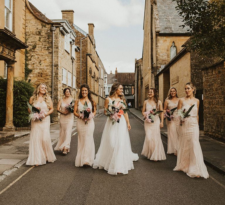 Bride walks with her bridesmaids down road as they hold tropical floral bouquets