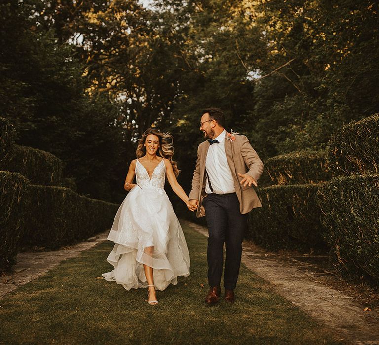 Bride & groom walk down a road on their wedding day as they hold hands and smile