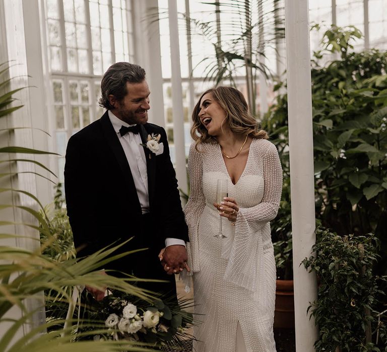 Groom in a black suit and bow tie laughing with his bride in an embellished wedding dress at Tatton Park 