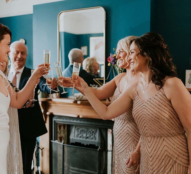 Bride raises a glass with her bridesmaids on wedding day who wear sparkling dresses