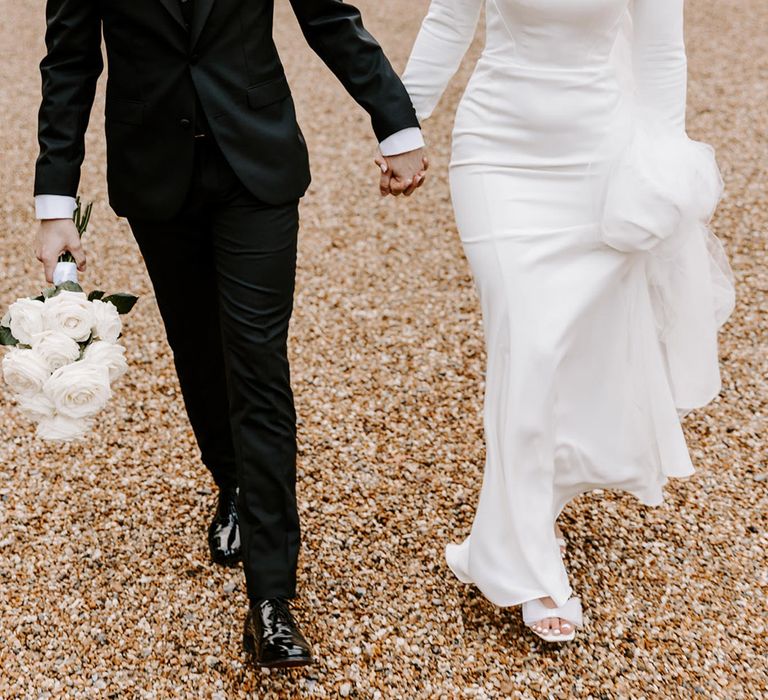 Groom in a black suit holding hands with his bride in a mermaid Essense of Australia wedding dress with detachable long sleeves at Northbrook Park 