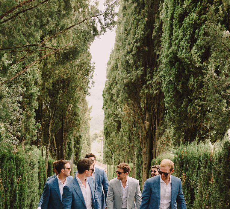 Groom walks with his groomsmen who wear white shirts and blue suits with no tie