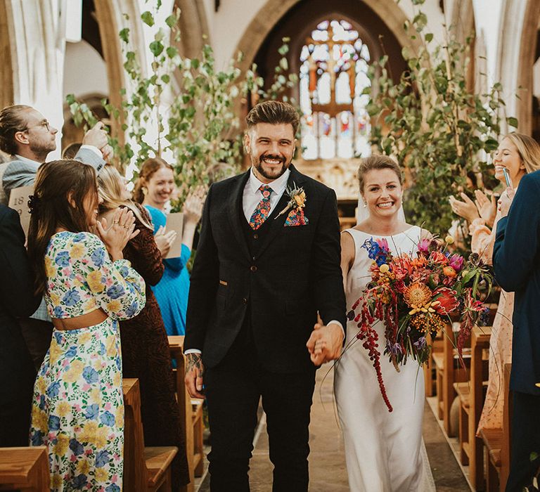 Church wedding ceremony with groom in a navy suit and floral tie and bride in a Charlie Brear Wedding dress with vibrant wedding bouquet 