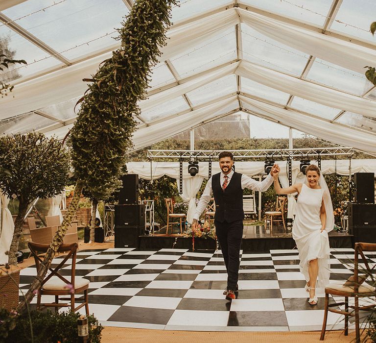 Bride and groom entering their back garden clear marquee wedding reception across the black and white dance floor 