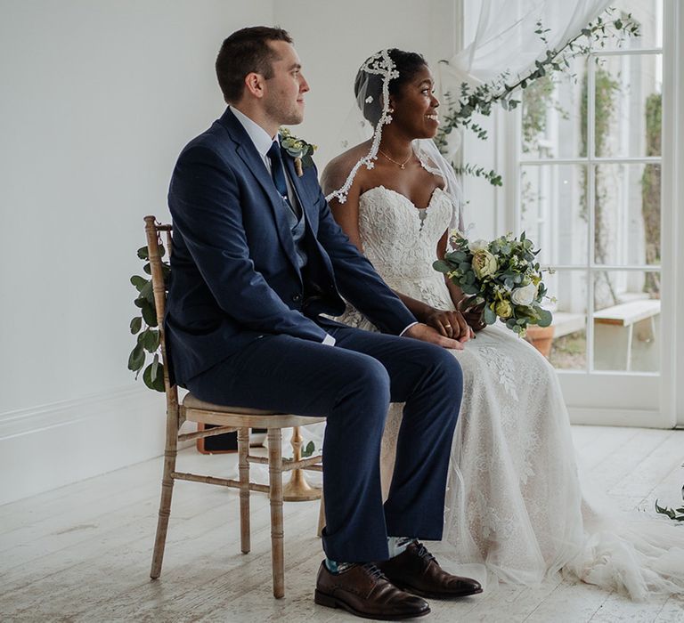 Bride wears lace edge wedding veil as she sits and holds hands with Groom in stunning rustic ceremony 