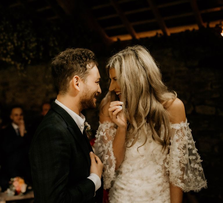 Groom in dark suit with floral buttonhole laughs with bride in boho wedding dress during rustic wedding ceremony in Hereford