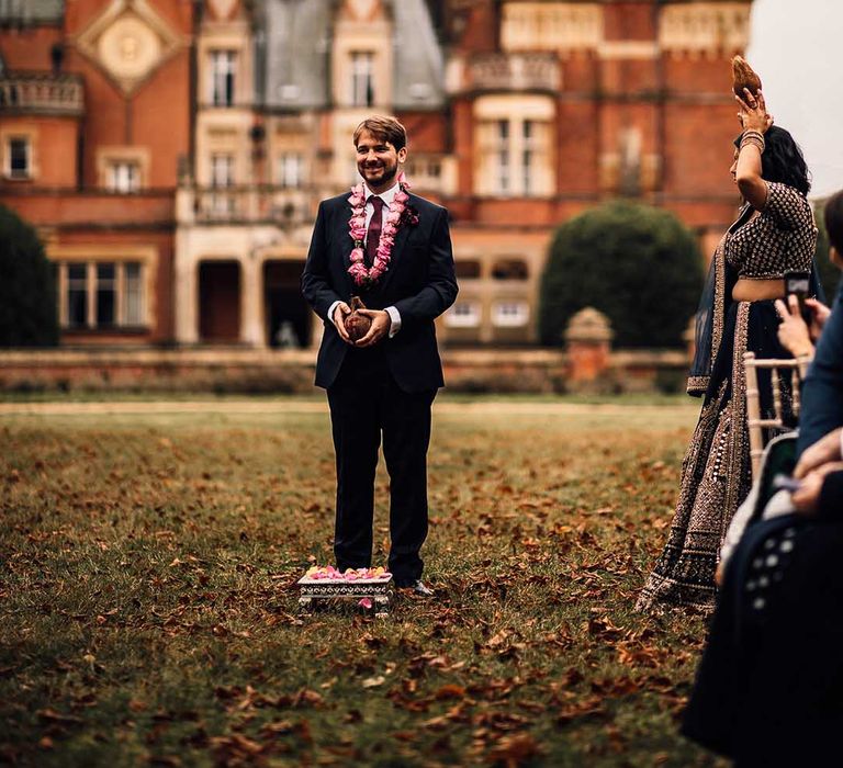 Groom wears dark suit with burgundy tie and pink flowers at Minley Manor 