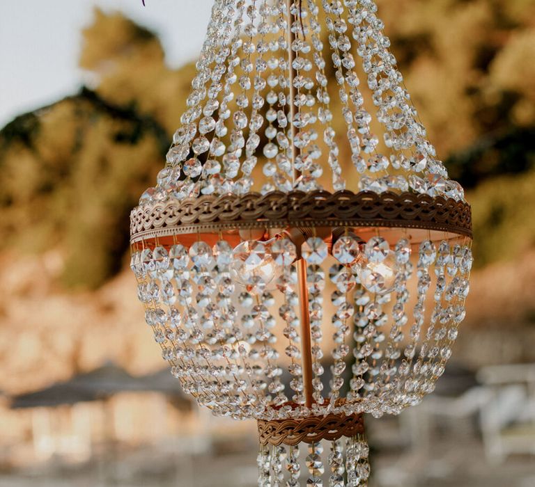 Chandelier hangs above wooden tables for outdoor wedding in Greece 