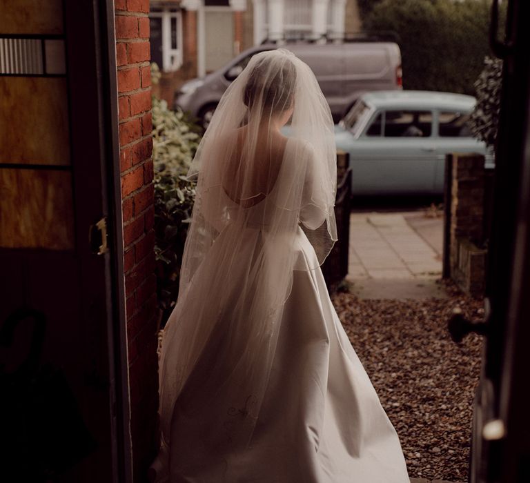 Bride in scoop back wedding dress and cathedral length veil walks to vintage blue wedding car