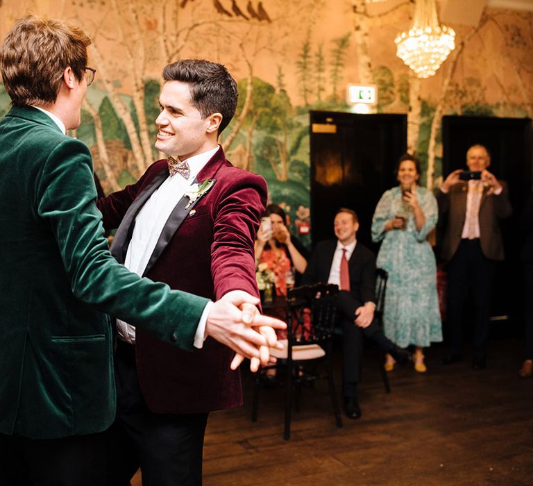 Two grooms in velvet tuxedo jackets share their first dance on their wedding day