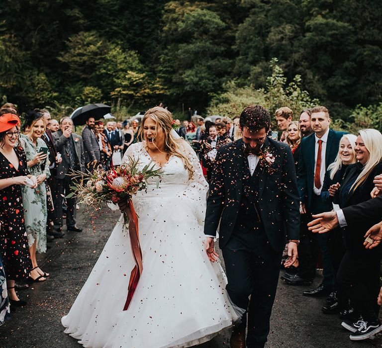 Confetti moment with curvy bride in a princess wedding dress and groom in a navy three-piece suit