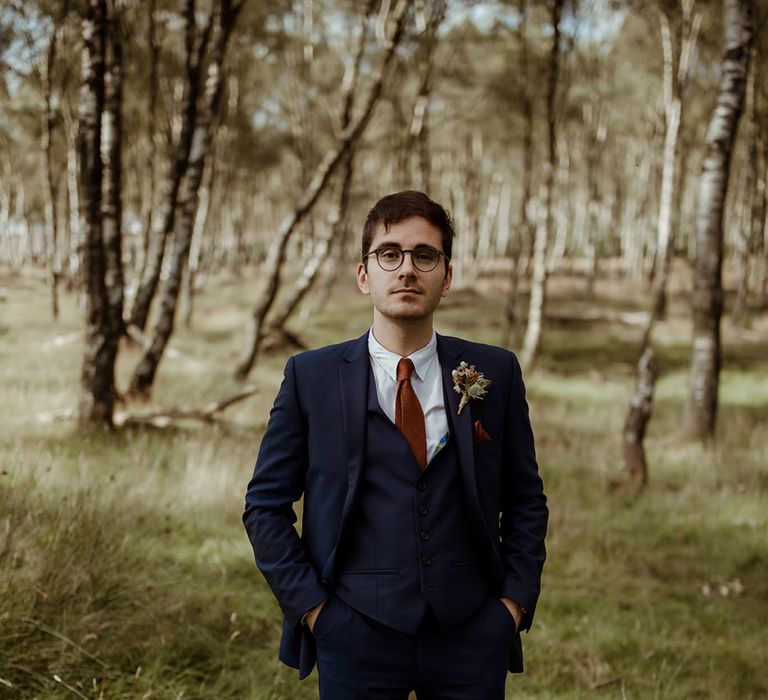 Groom in navy blue three piece suit with rust coloured tie and handkerchief with autumnal buttonhole