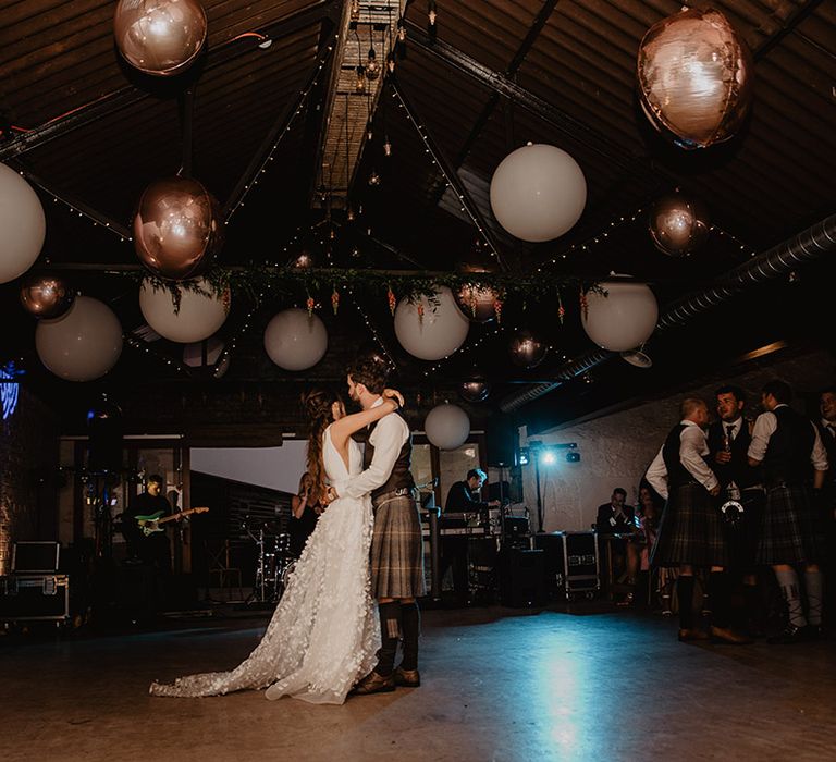 Bride and groom have their first dance under fairy lights and large white and rose gold ballon decoration at Cardney Estate