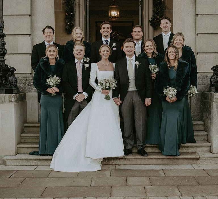 Wedding party, bride in Suzanne Neville long wedding dress, bridesmaids in bottle green Suzanne Neville long bridesmaids dresses and black cropped fur coats