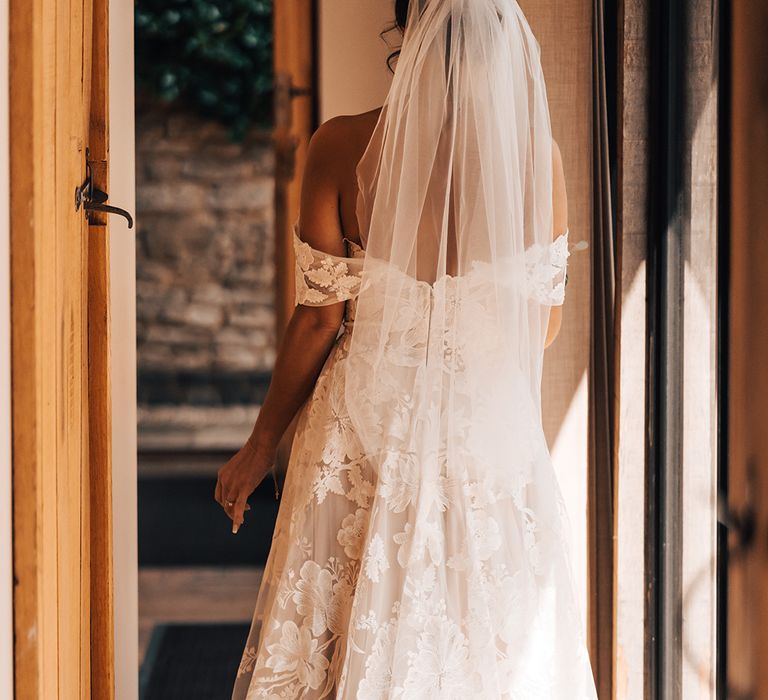 Lace floral off the shoulder wedding dress worn by bride with veil and gold leaf hair accessory