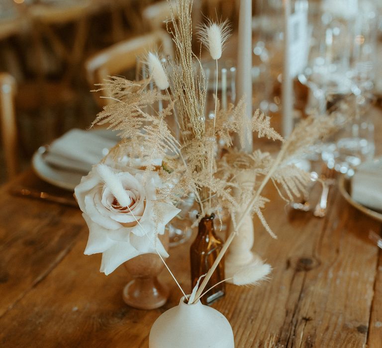 Cream vases and coloured glass vases full of rose flower arrangement with tea lights for table decoration at boho wedding