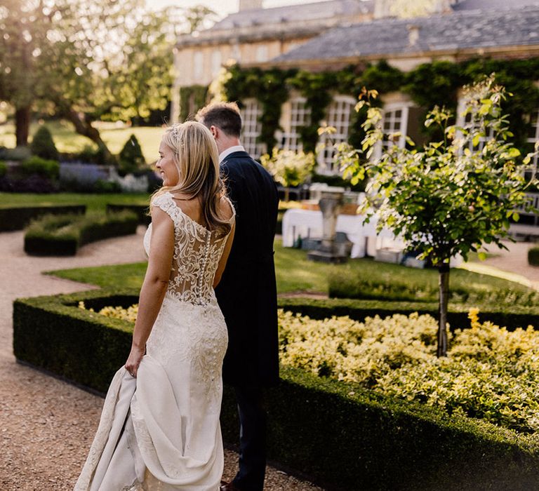 Bride in sheer lace back wedding dress with button detail walking around gardens at Goldney Hall with groom 