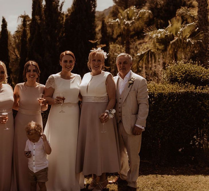 Bride stands with wedding party and bridesmaids who wear pale pink gowns complete with capped sleeves 