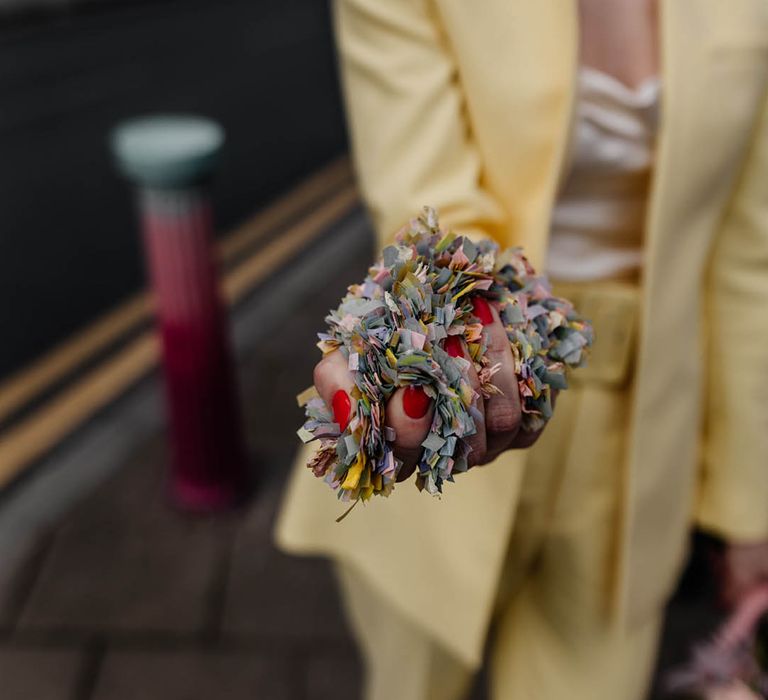 bridesmaids in a yellow trouser suit holding colourful confetti in her hands with red nail polish 