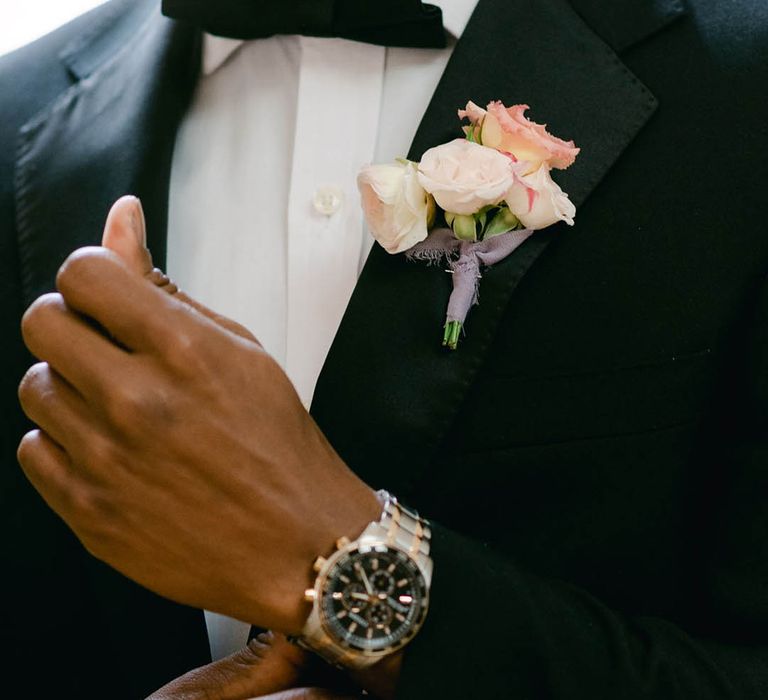 Groom wears black tie for the wedding with a pink flower buttonhole tied with purple ribbon 