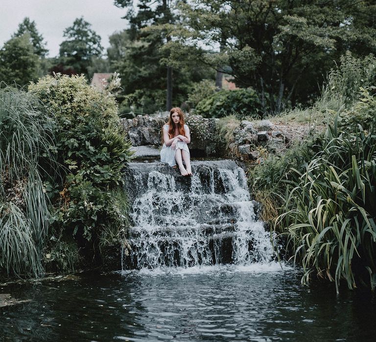 Beautiful bride with long hair and natural makeup sitting in the moat at Bishop's Palace, Wells