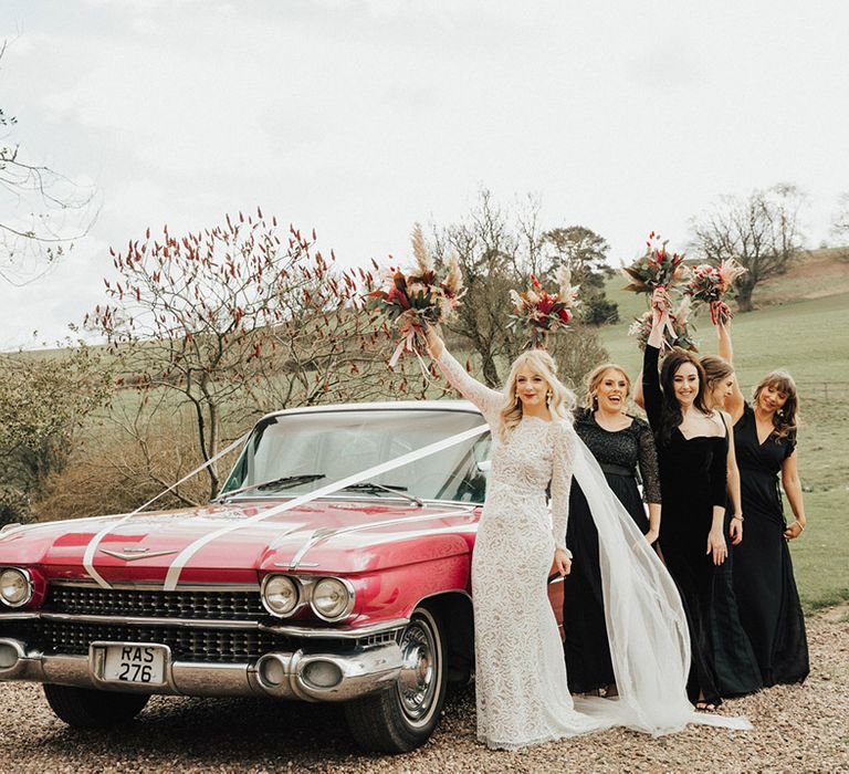 Vintage pink Cadillac with a white ribbon wedding car with the bride and her party in different styles of black dresses