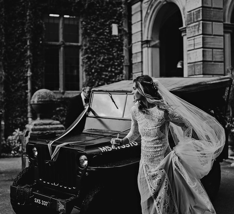 Bride in a boho lace wedding dress with a long veil getting into the Jeep wedding car 