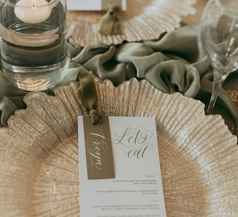 Green and white wedding menu on gold chargers with sage green runners and floating tea lights 