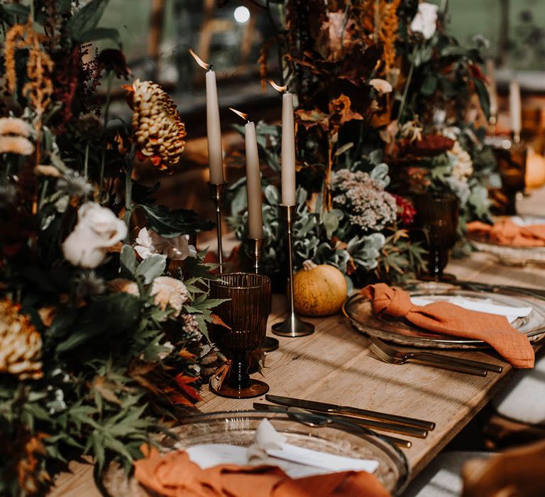 Clear charger plates with orange napkins, coloured glassware, mini pumpkins and dark flowers 