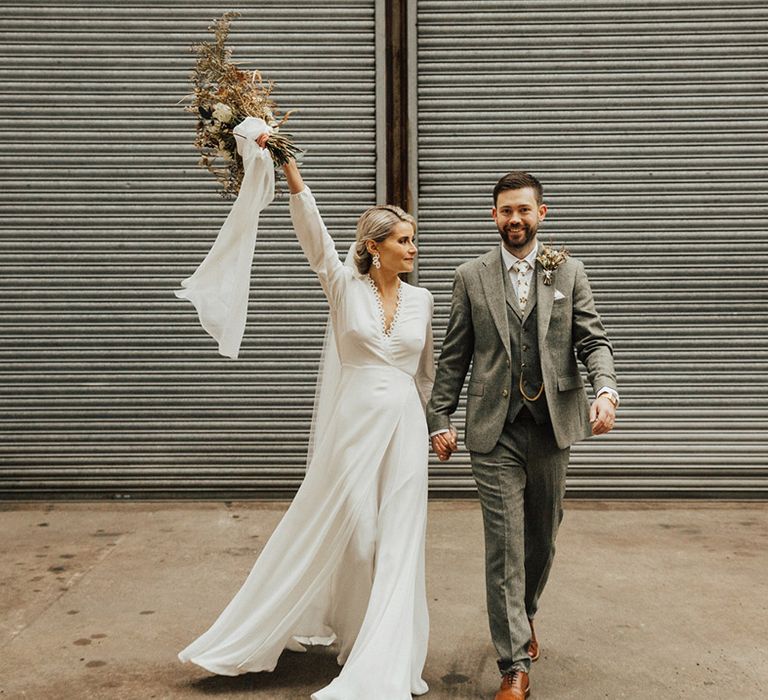 Bride wears long sleeve Reformation wedding dress and walks with her groom in three-piece grey suit 