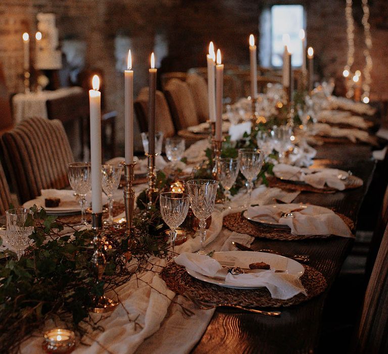 White table runner with foliage, wicker placemat, white and grey candles and crystal glassware for a cosy rustic winter wedding 