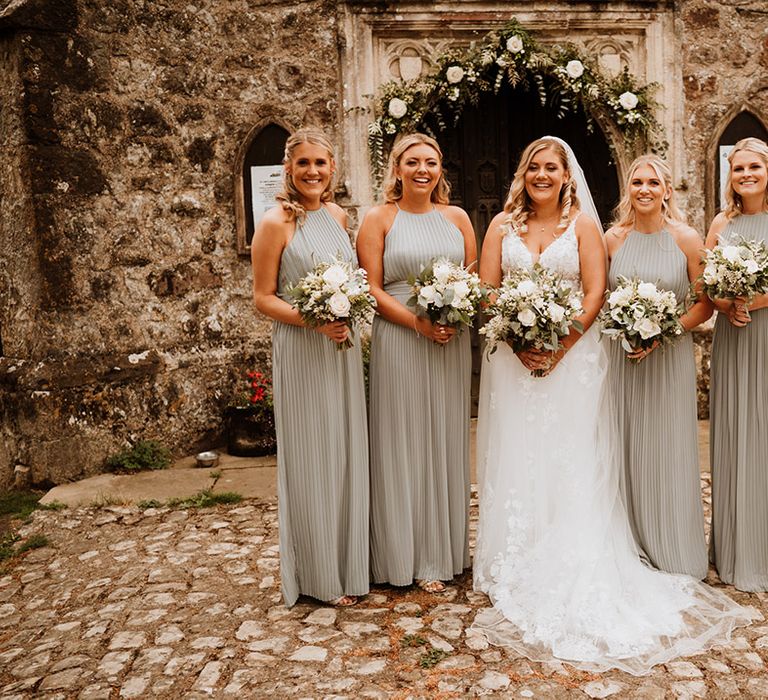 Bridesmaids in sage green halter neck pleated bridesmaid dress with the bride in a flower lace gown 