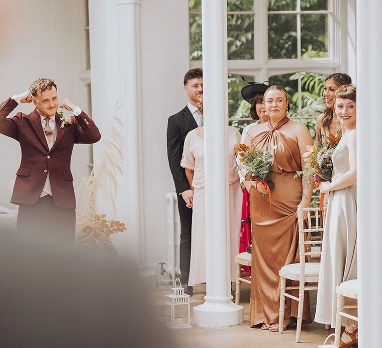 Groom wears maroon suit with grey waistcoat and floral buttonhole 