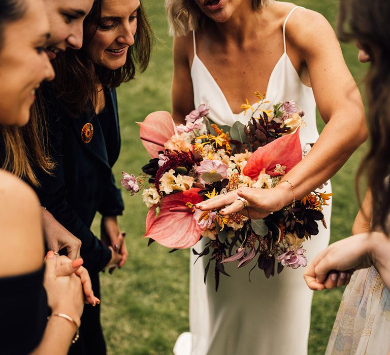 Bride holds tropical bridal bouquet with bright florals and shows her wedding ring