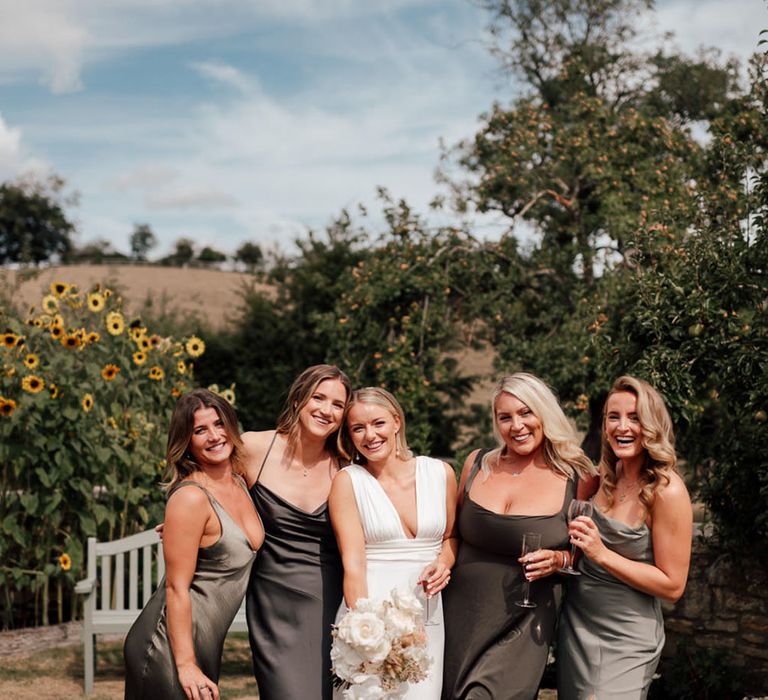 Blonde bride with pearl earrings with plunging wedding dress holding a white orchid bouquet with the bridesmaids in mismatched dresses 